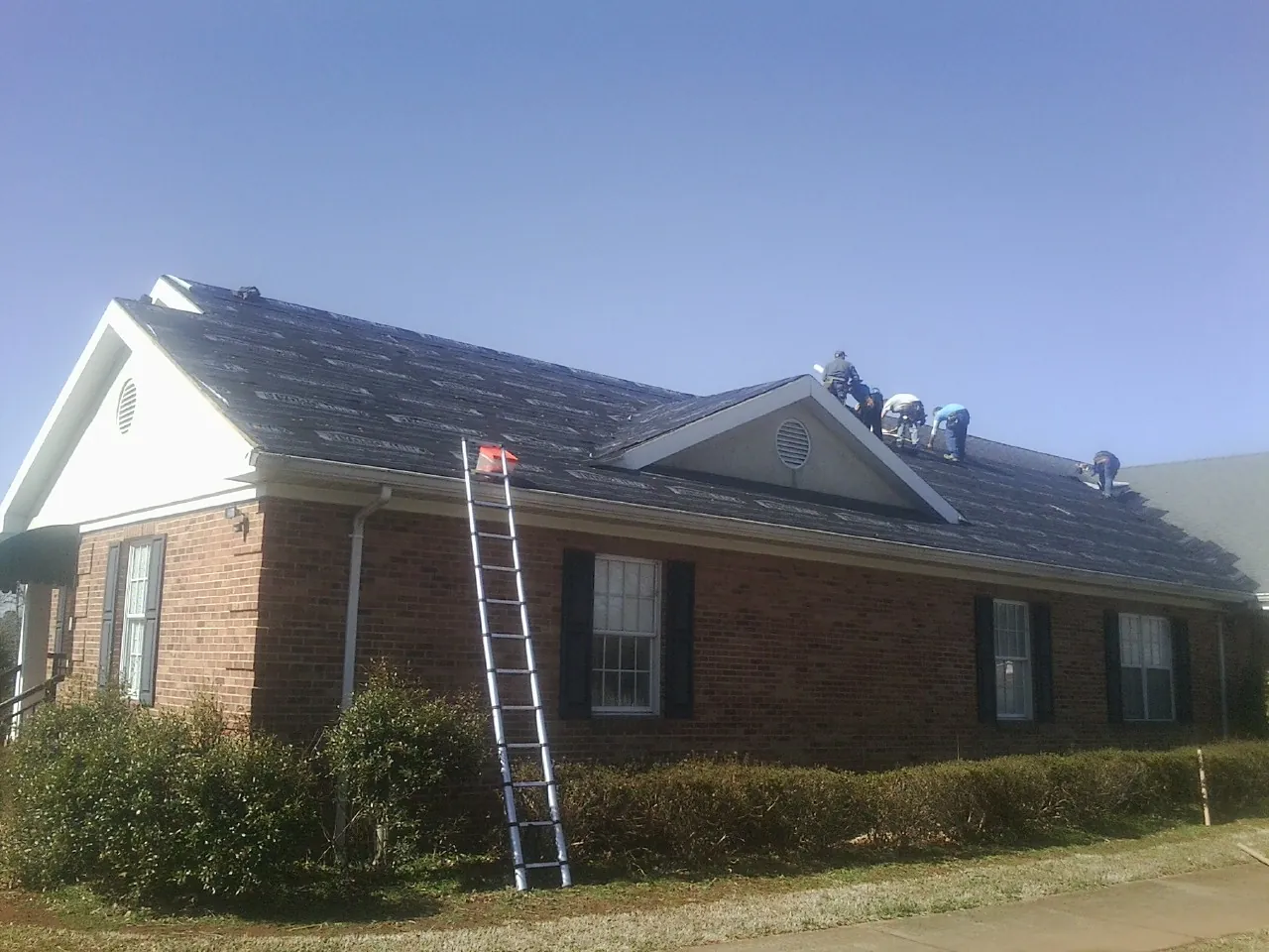 Crew tearing shingles off a brick ranch roof with a ladder set — Emergency Roof Repair work by our crew in La Grange