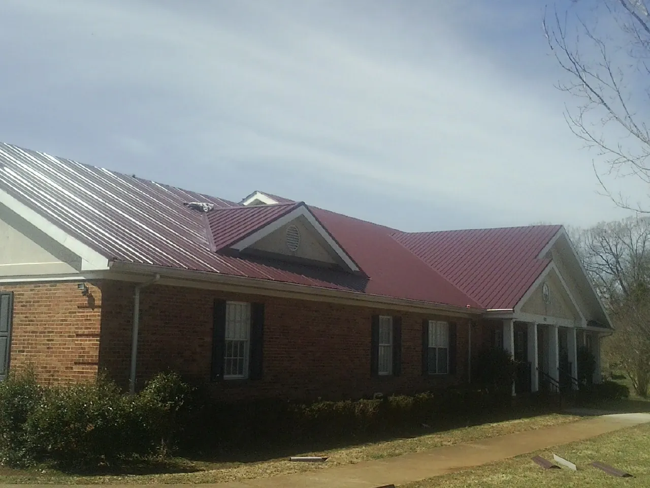 Red metal roof with gabled entries on a long brick building, from a Hail Damage Roof Repair job in La Grange