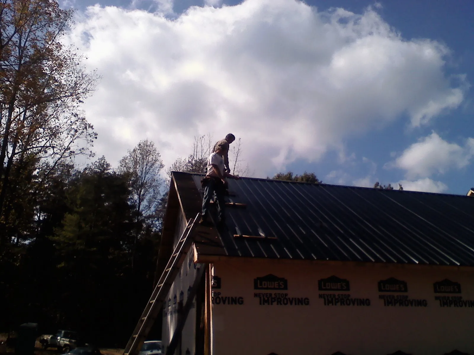 Roofer fastening dark metal panels high against a cloudy sky, from a Roof Inspection job in La Grange
