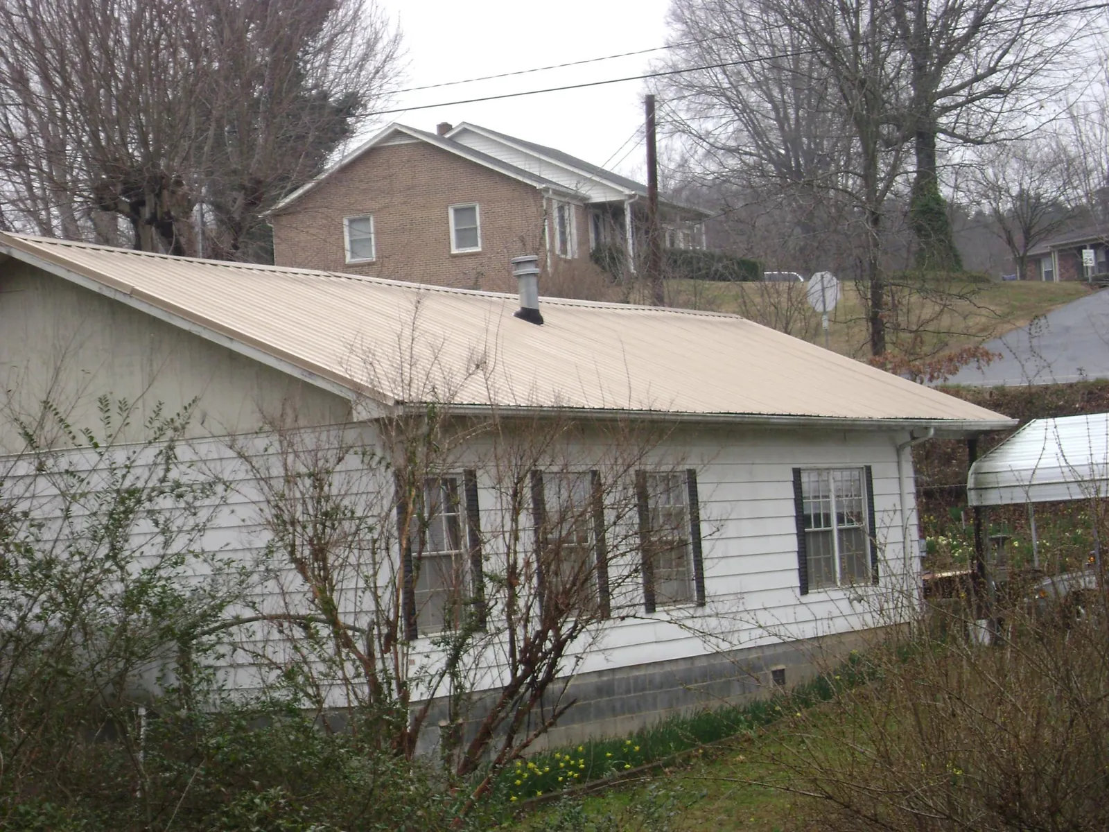 Tan metal roof on a white sided house set into a hillside — Commercial Roofing by Roofing Brothers in La Grange